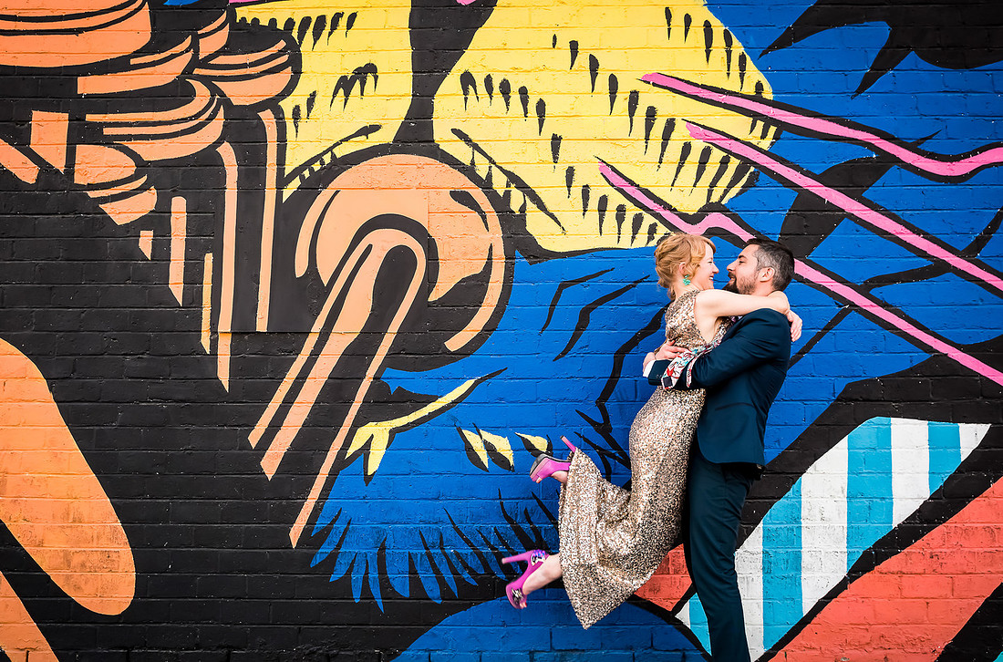 Couple embracing during a Las Vegas anniversary photo shoot in the Arts District with colorful mural backdrop.