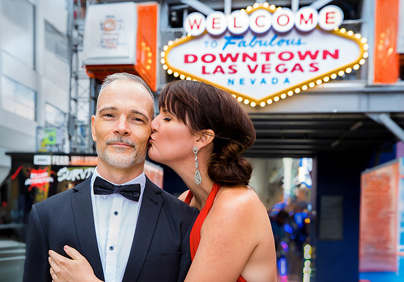 Couple posing beneath the Welcome to Downtown Las Vegas sign during an anniversary photo session.